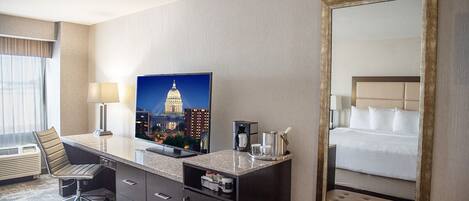 A hotel room with a desk, chair, bed, and a large mirror.