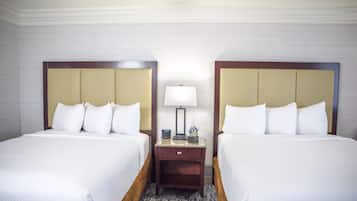 A hotel room with two beds, a nightstand with a lamp, and a small table with a vase.