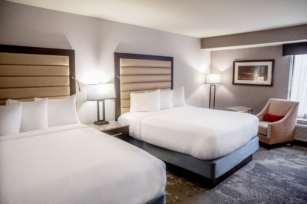 Habitación de hotel con dos camas, una silla, una lámpara y un cuadro en la pared.