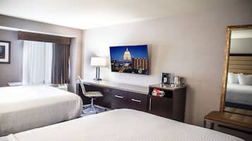 A hotel room with two beds, a desk with a lamp, a coffee maker, and a painting of a cityscape.