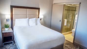 Camera d'albergo con un letto grande, un comodino con una lampada, una pianta in vaso e un box doccia in vetro.