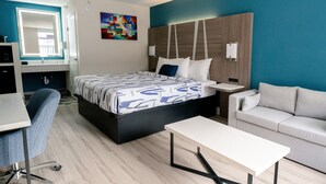 A modern hotel room with a bed, a desk, a chair, a sofa, and a painting on the wall. - Serenity Stay (Chattanooga)