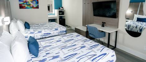 A hotel room with two beds, a desk, a TV, a mirror, and a bathroom with a sink and mirror.