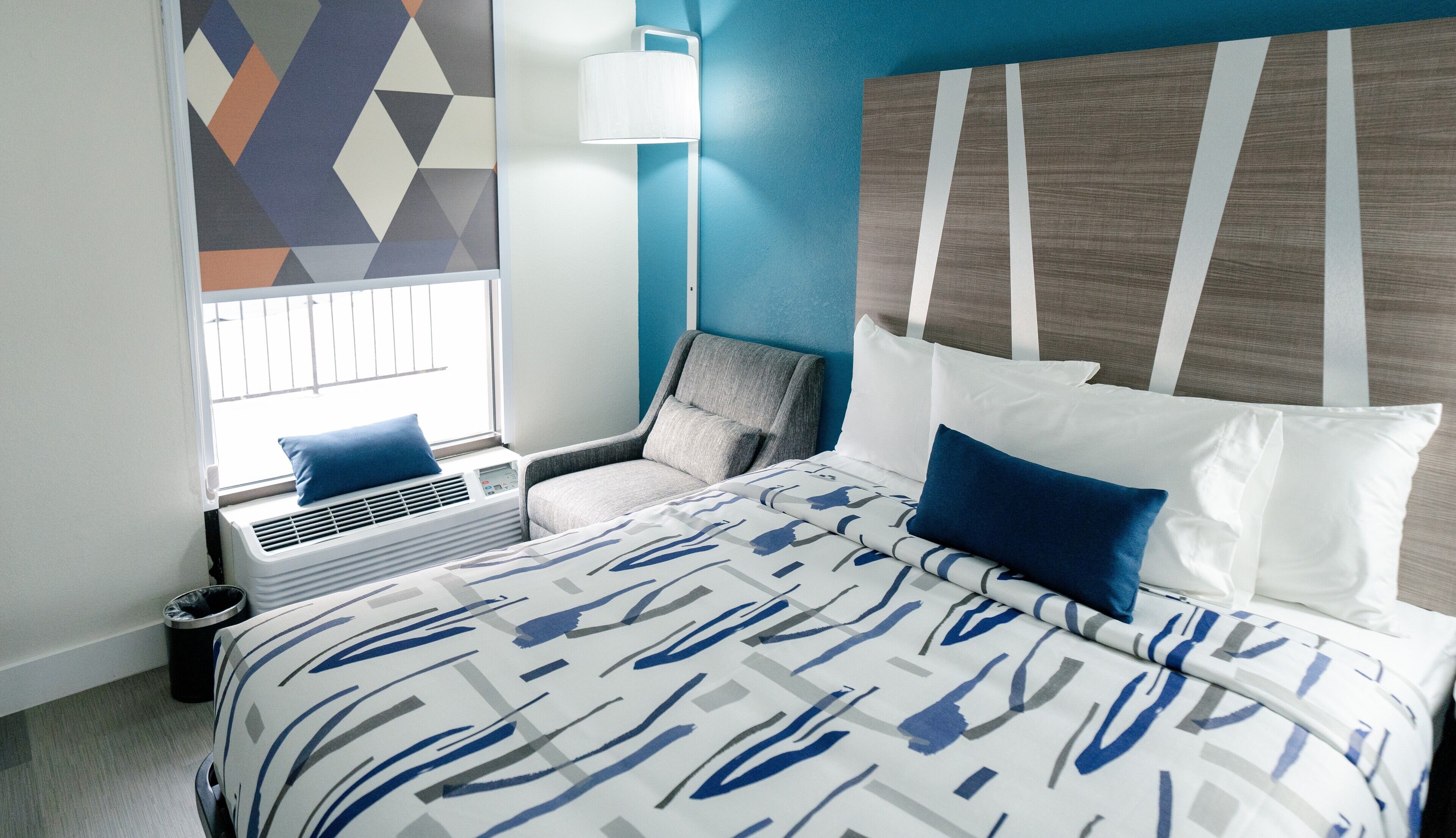 Une chambre d’hôtel avec un lit, une chaise, une fenêtre et un mur orné d’un motif géométrique.