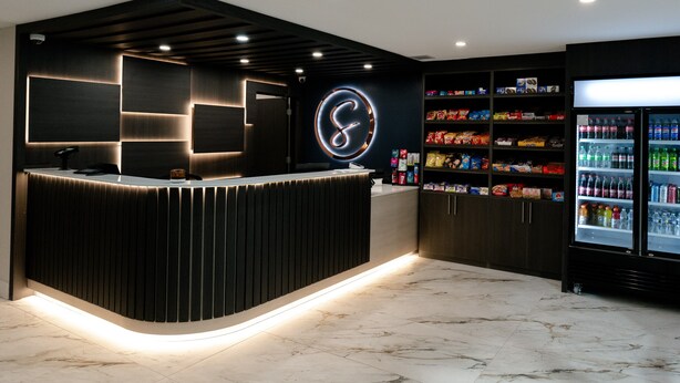 A reception area with a modern design, featuring a curved reception desk, a large illuminated logo on the wall, and a snack vending machine. - Serenity Stay (Chattanooga)
