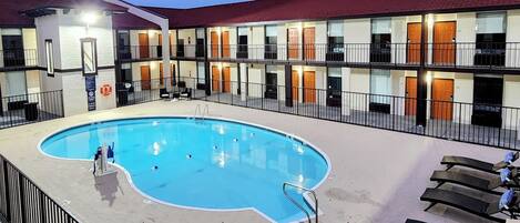 A hotel with a swimming pool, multiple balconies, and a red roof.