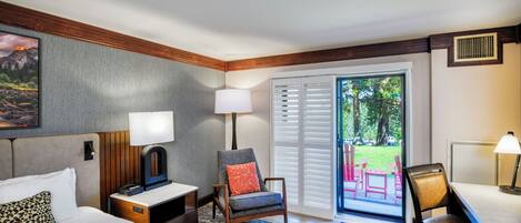 A hotel room with a bed, two chairs, a desk, a lamp, and a view of the outdoors.