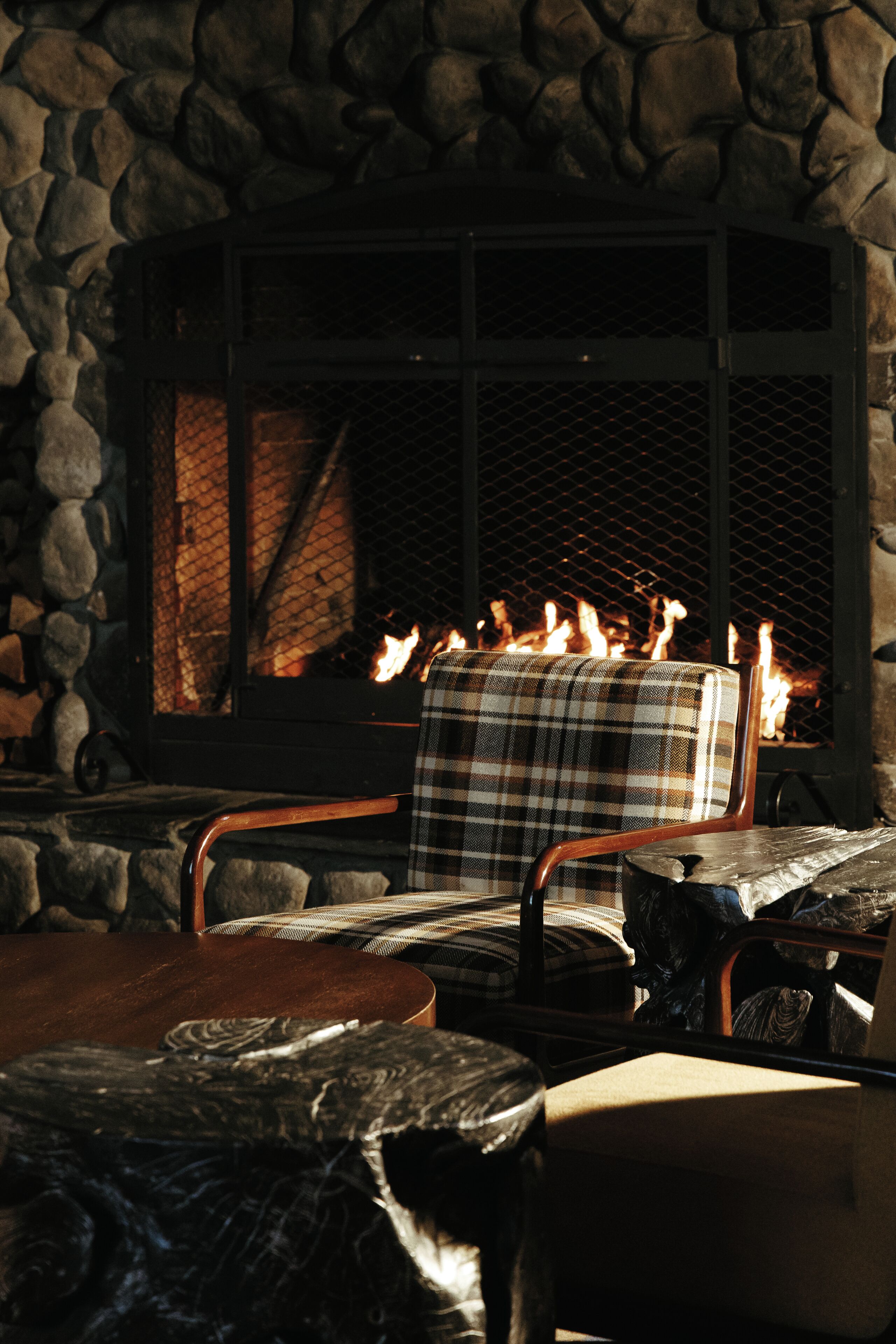 Una chimenea de piedra con una manta escocesa sobre una silla, una mesa de madera y una pared de piedra.
