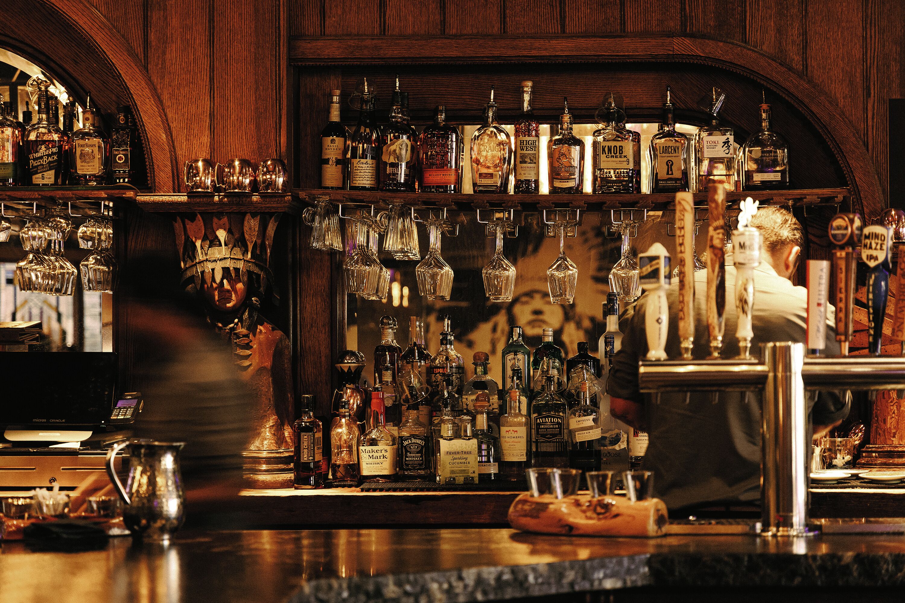 Un bar con una variedad de botellas de licor y un barman preparando bebidas.