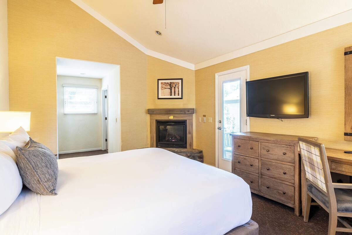 Una habitación de hotel con una cama grande, chimenea, televisor y escritorio con cajones.
