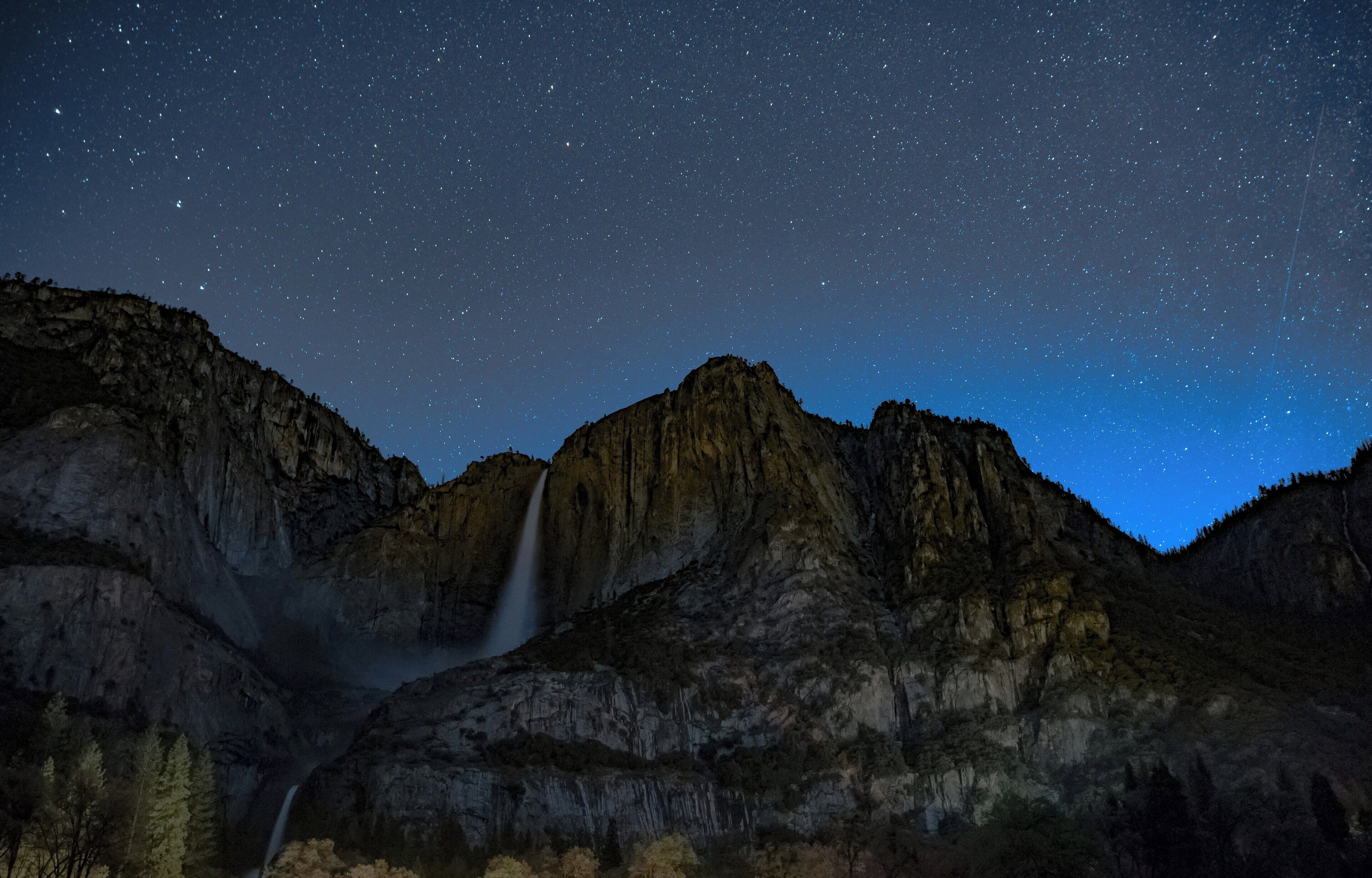 A night sky over a mountainous landscape with a waterfall.