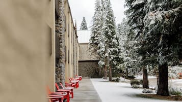 Ein verschneiter Außenbereich mit rotem Stühlen, die an einem Gebäude anreihen, umgeben von mit Schnee beladenen Bäumen.