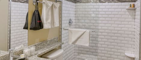 Un baño moderno con encimera de granito, inodoro blanco, ducha con mampara de vidrio y espejo con toallero.