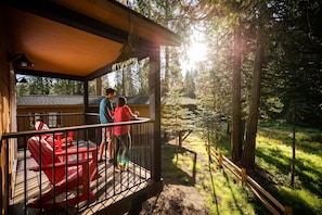 A wooden deck with a red Adirondack chair, a covered seating area, and a view of a forested area. - Tenaya at Yosemite (Fish Camp)