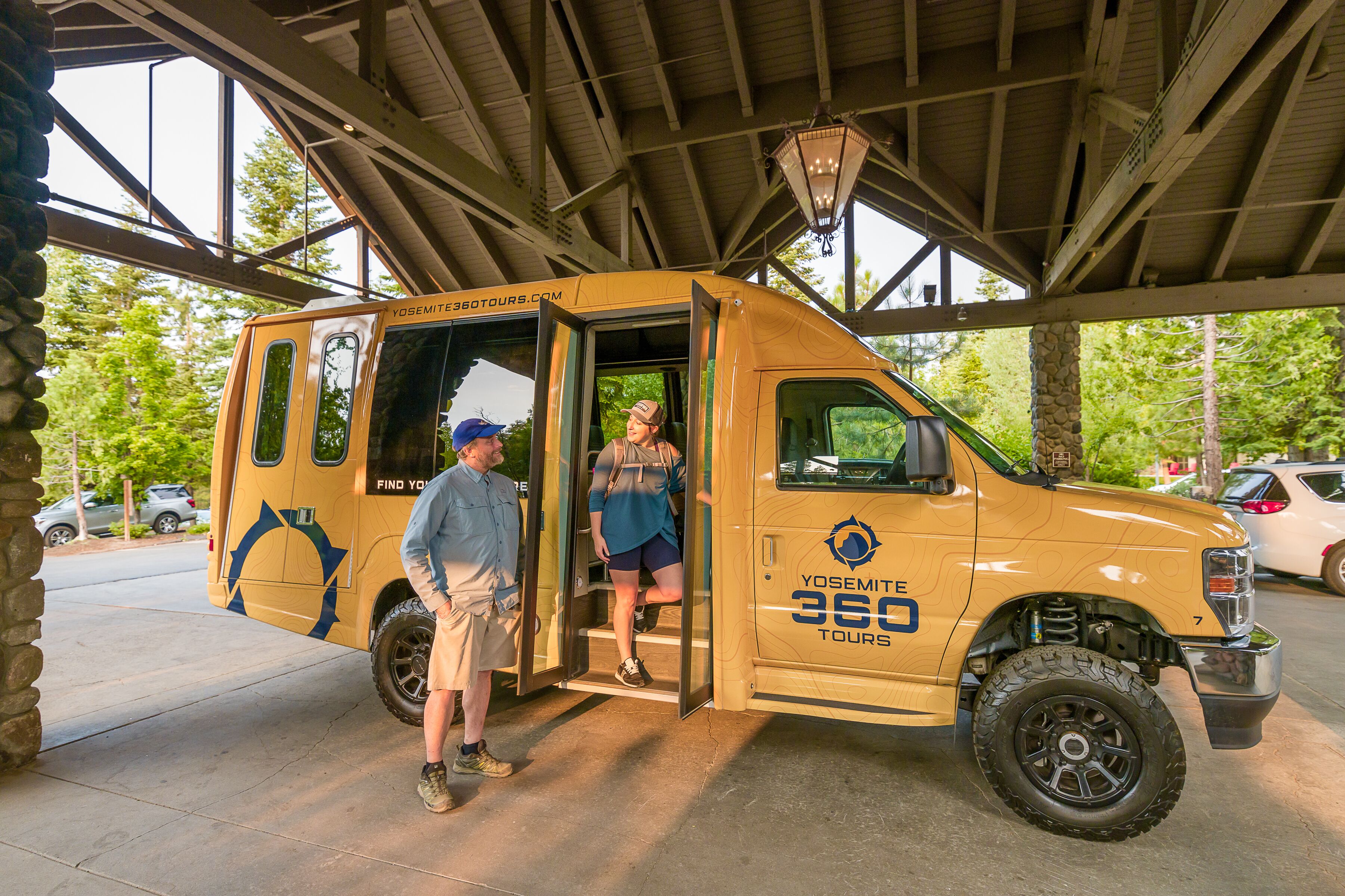 A yellow tour bus with the text "Yosemite 360 Tours" parked under a covered area with stone pillars.