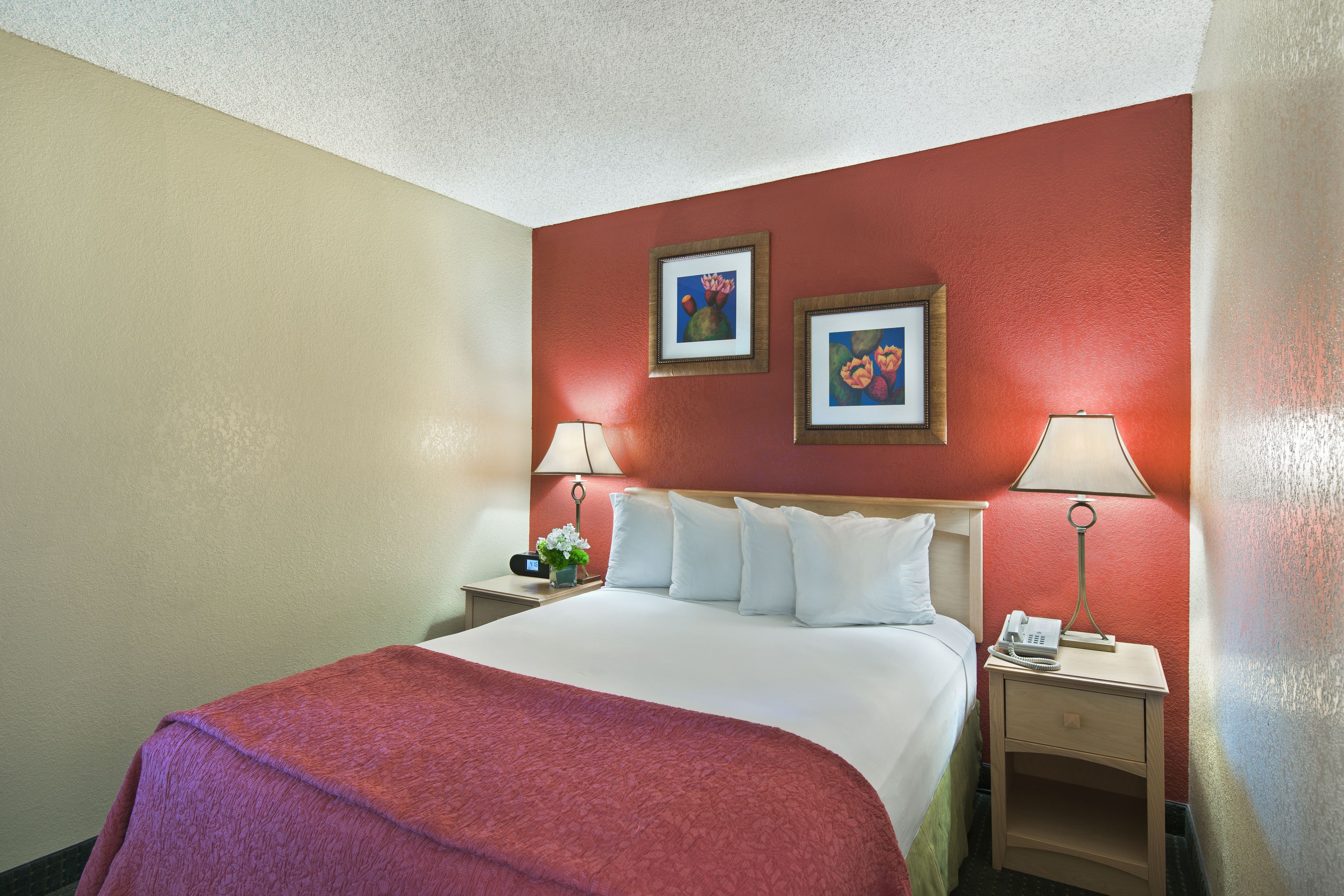 A hotel room with a bed, two bedside tables, a nightstand, a lamp, and two framed pictures on the wall.
