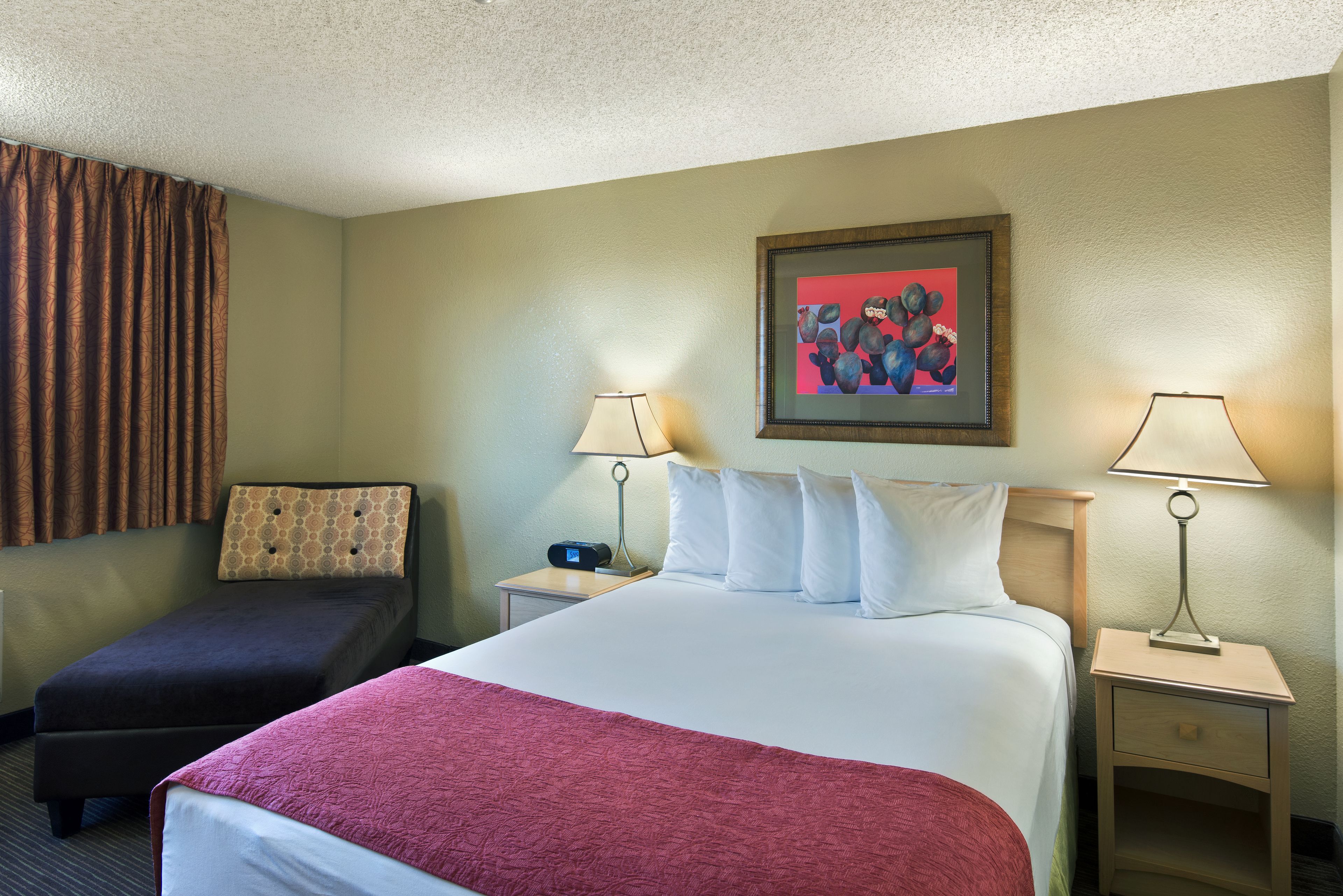A hotel room with a large bed, a smaller sofa, two bedside tables with lamps, and a framed picture on the wall.