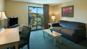 Quarto de hotel com televisão, sofá, mesa de centro e vista para uma varanda com mobiliário de exterior.