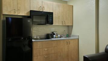 Cocina compacta con refrigerador negro, microondas y armarios de madera.