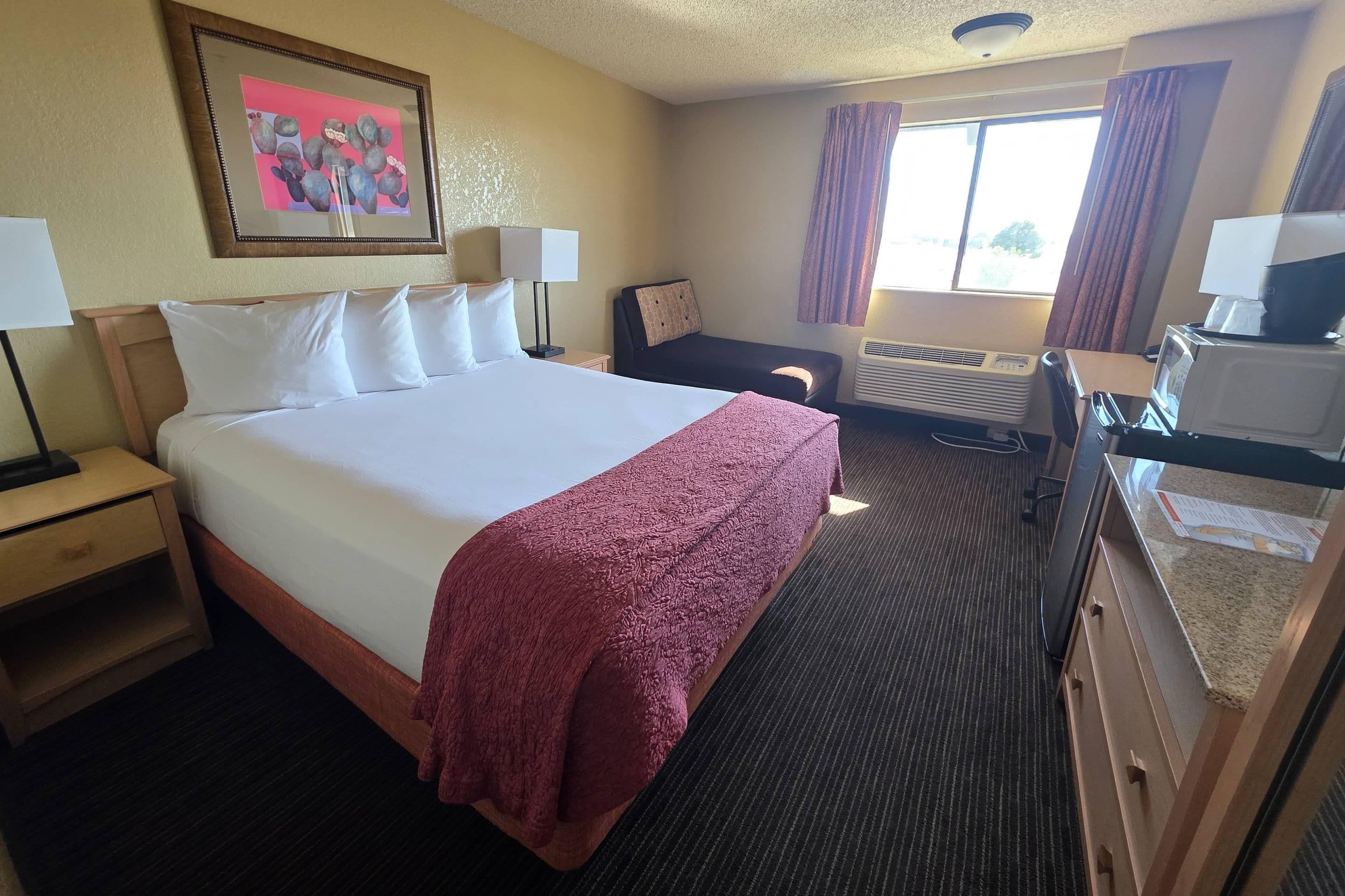 A hotel room with a large bed, a desk with a computer, a microwave, and a window with curtains.
