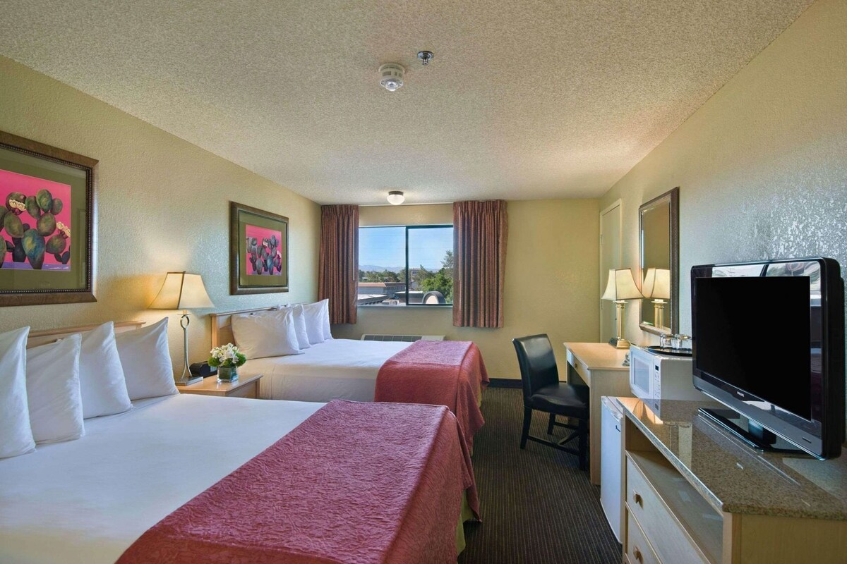 A hotel room with two beds, a desk with a television, a chair, and a window with curtains.