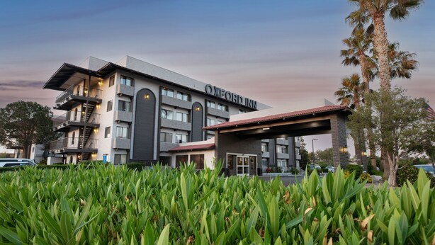 Um hotel moderno com telhado plano e várias varandas, e uma placa com a inscrição "OXFORD INN".