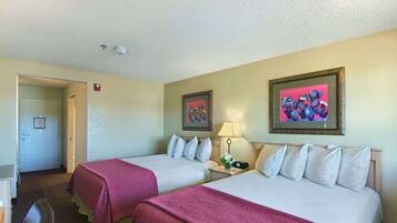 A hotel room with two beds, each with a pink bedspread and white pillows. There is a nightstand with a lamp and a framed picture on the wall.