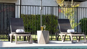 Duas poltronas perto de uma piscina, com uma mesa e uma taça de champanhe.