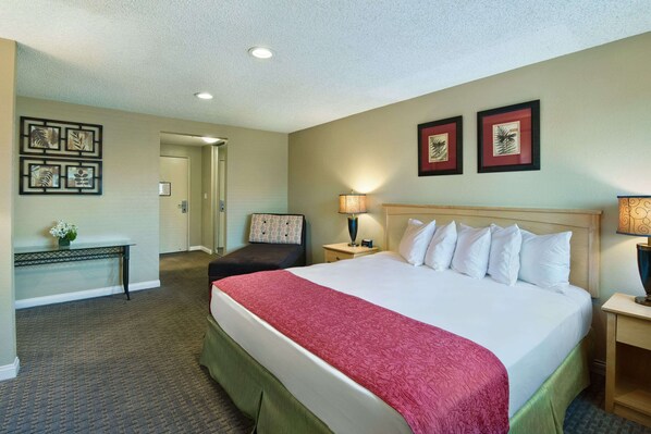 Relax in a spacious room with a large bed, nightstand, and comfortable chair, surrounded by framed artwork.