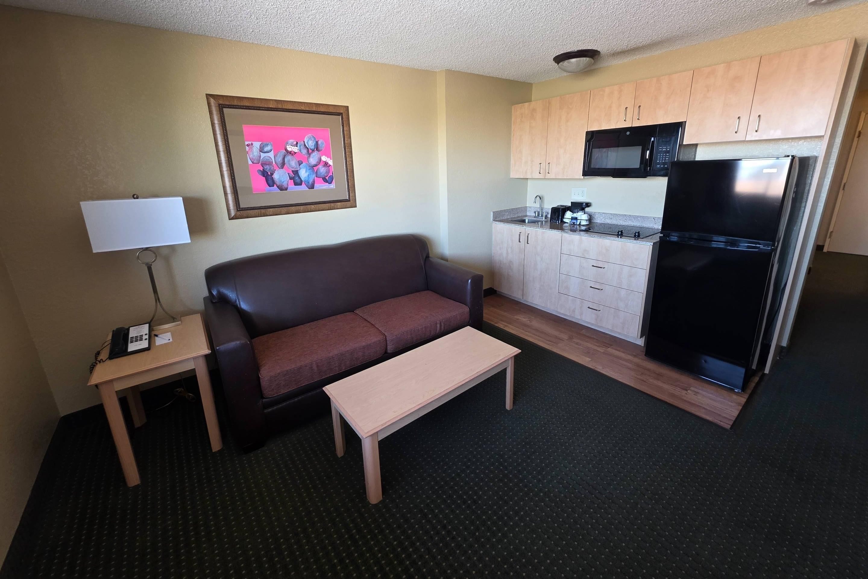A compact living space with a sofa, a small table, a kitchenette with a refrigerator, microwave, and coffee maker.