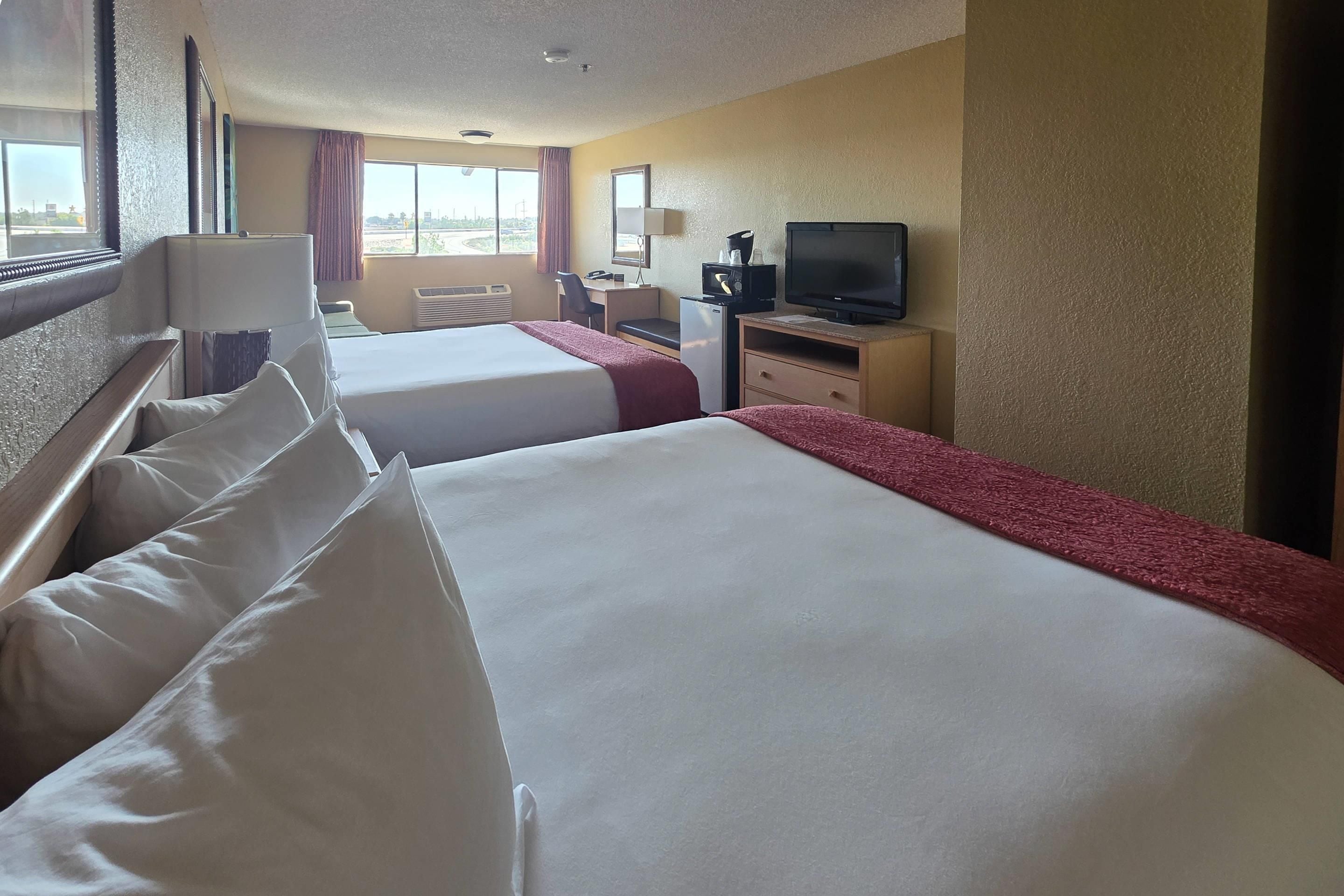 Una habitación de hotel con dos camas, un escritorio, un televisor y una ventana con cortinas.