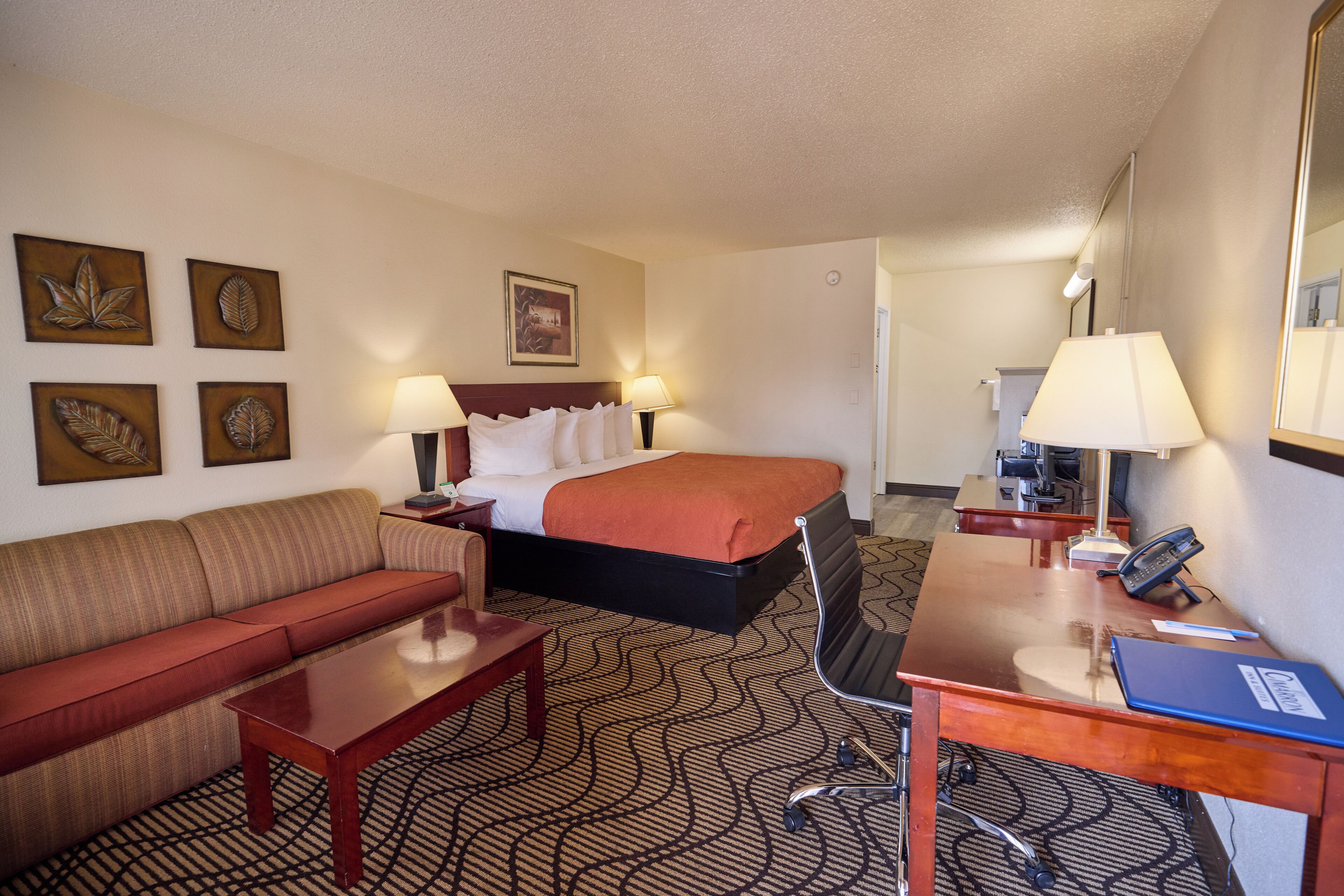 Une chambre d’hôtel avec un lit, un canapé, un bureau et une chaise. On y trouve également des œuvres d’art accrochées au mur et une lampe sur le bureau.