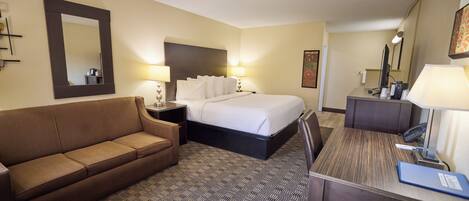 A hotel room with a bed, a sofa, a desk, and a mirror.
