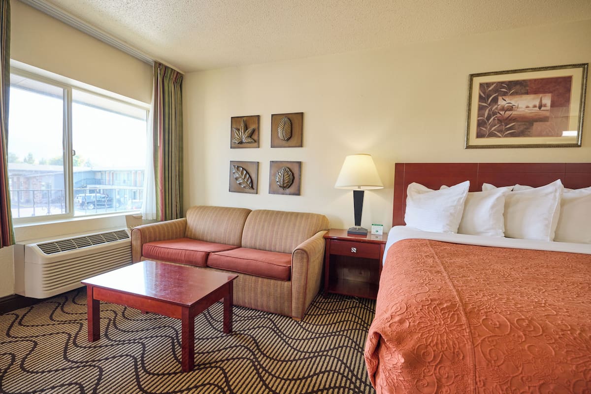 Une chambre d’hôtel avec un lit, un canapé, une table, une lampe et une fenêtre avec des rideaux.