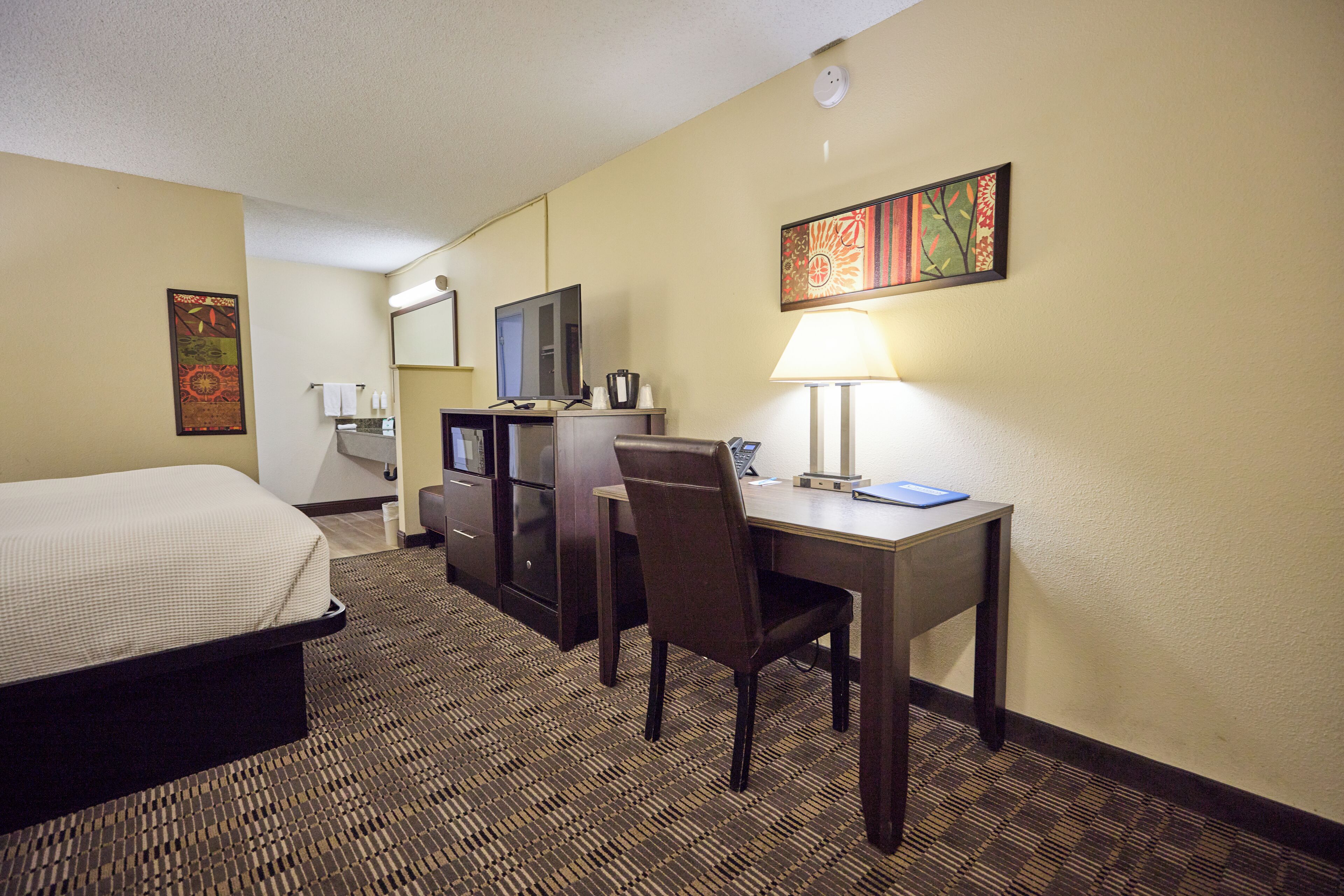 Ein Hotelzimmer mit Bett, Schreibtisch, Stuhl, Lampe, Fernseher und Wandbild.