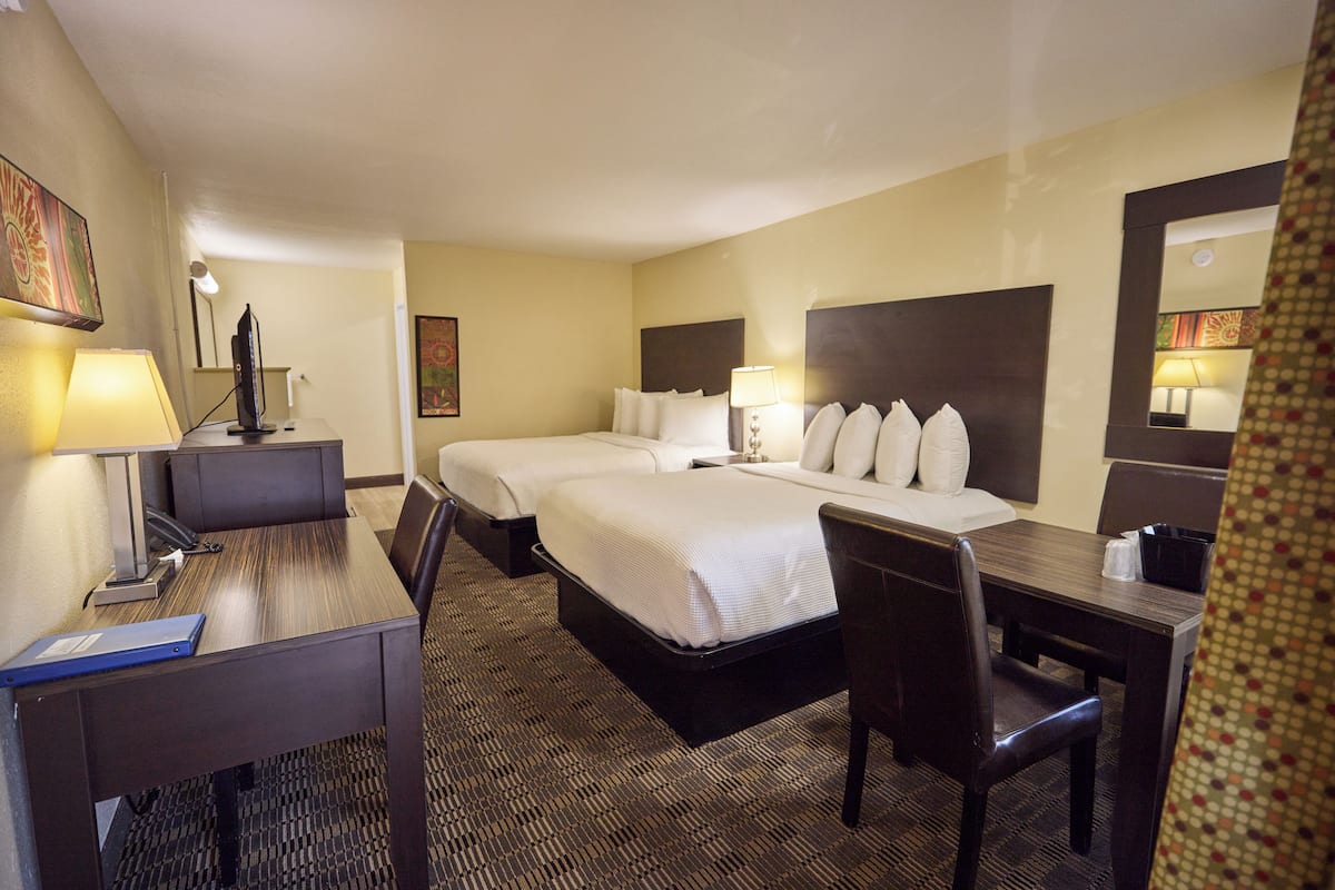 Une chambre d’hôtel avec deux lits, un bureau, une chaise, une lampe et un miroir.