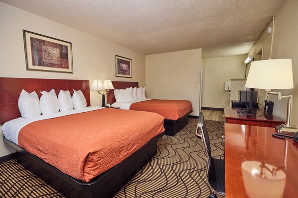 A hotel room with two beds, a desk, and a mirror.