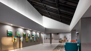 A spacious lobby with a high ceiling, a reception desk, and a row of artwork on the wall. - The Anaheim Hotel (Anaheim)