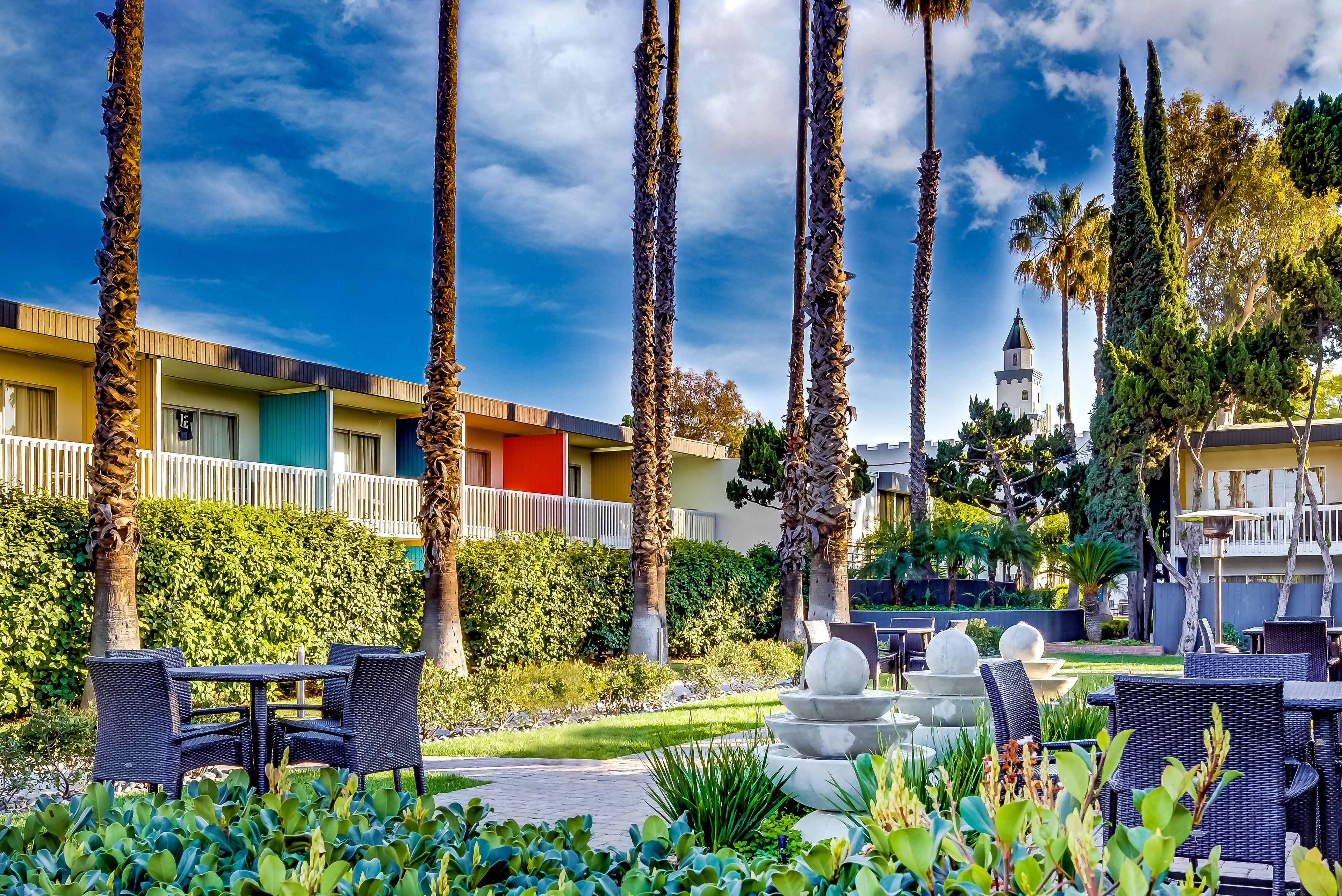A hotel courtyard with outdoor seating, palm trees, and a view of a distant building.