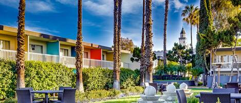A hotel courtyard with outdoor seating, palm trees, and a view of a distant building.