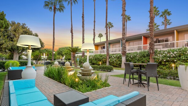 A hotel courtyard with outdoor seating, palm trees, and a building with balconies. - The Anaheim Hotel (Anaheim)