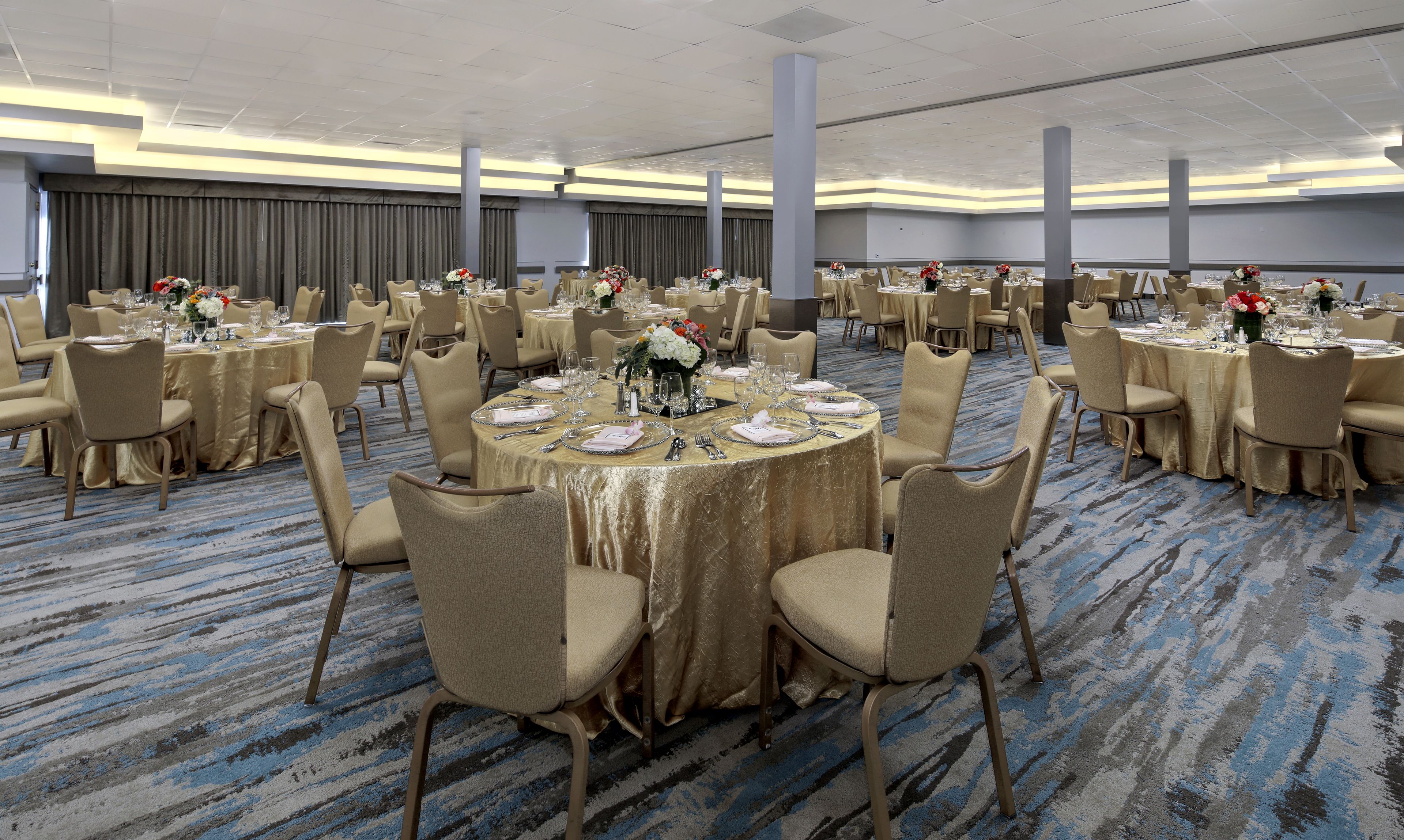 A banquet hall with round tables, beige chairs, and gold tablecloths.