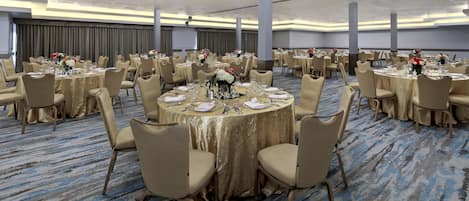 A banquet hall with round tables, beige chairs, and gold tablecloths.
