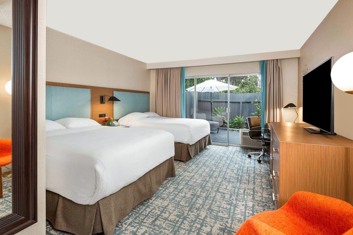 A hotel room with two beds, a desk, a television, and a view of the outdoors.