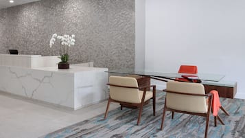 A reception area with a marble counter, a potted orchid, two beige chairs, and a glass table.