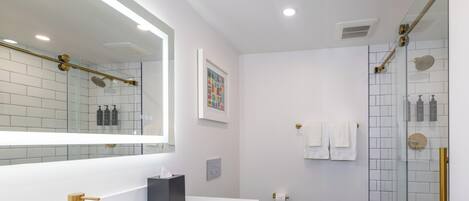 Une salle de bain moderne avec un lavabo blanc, des robinetteries dorées, une douche en verre et un sol carrelé.