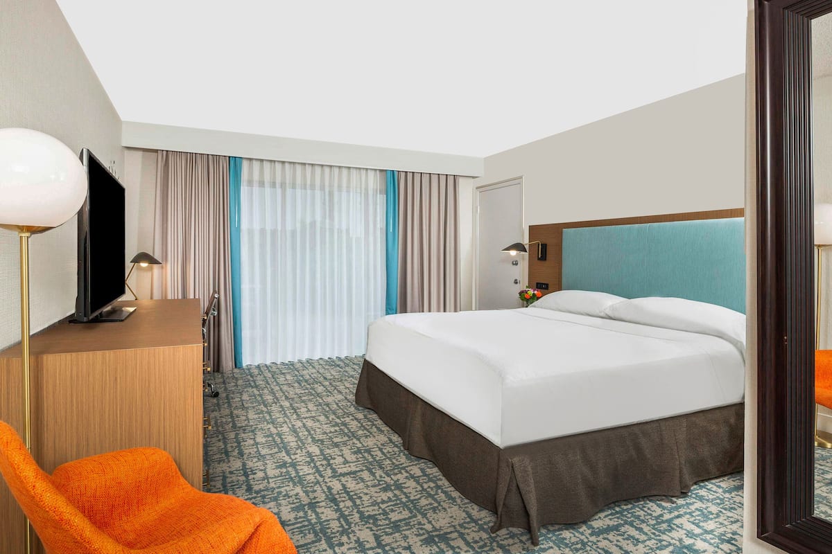 A hotel room with a large bed, a desk with a television, a chair, and a window with curtains.