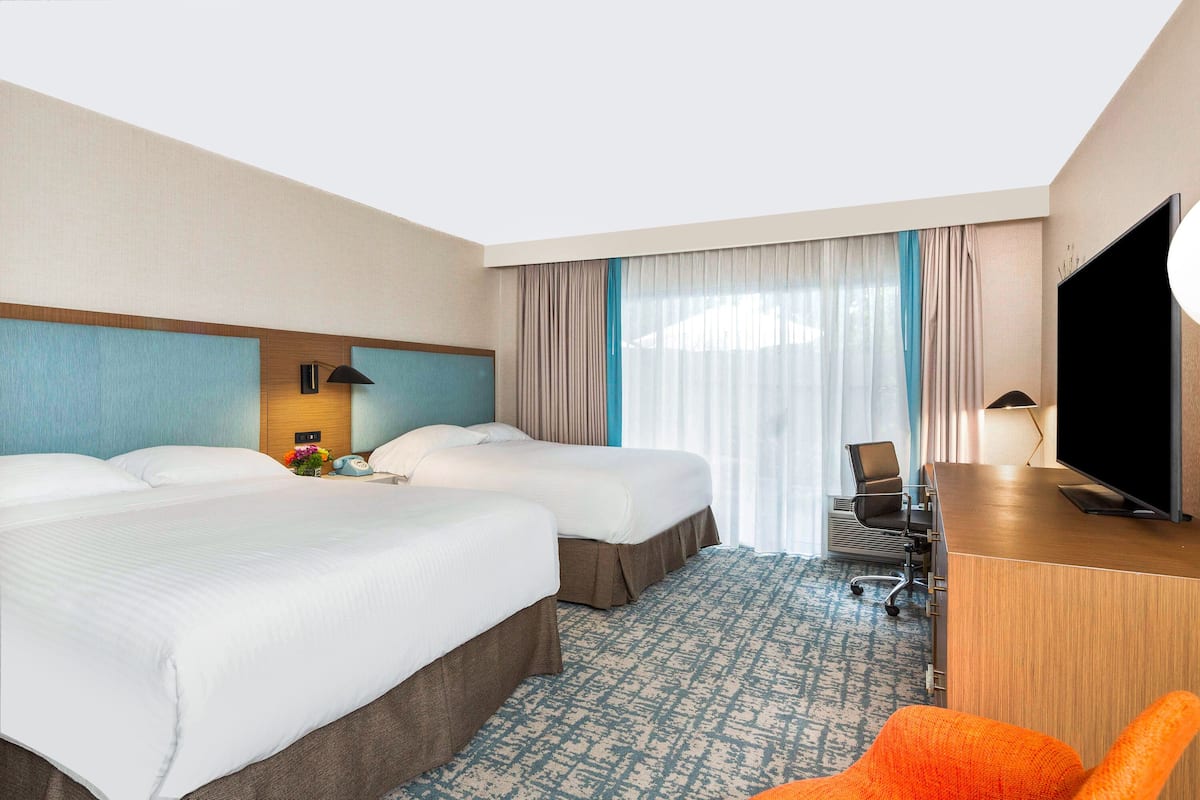 A hotel room with two beds, a desk with a TV, a chair, and a patterned carpet.