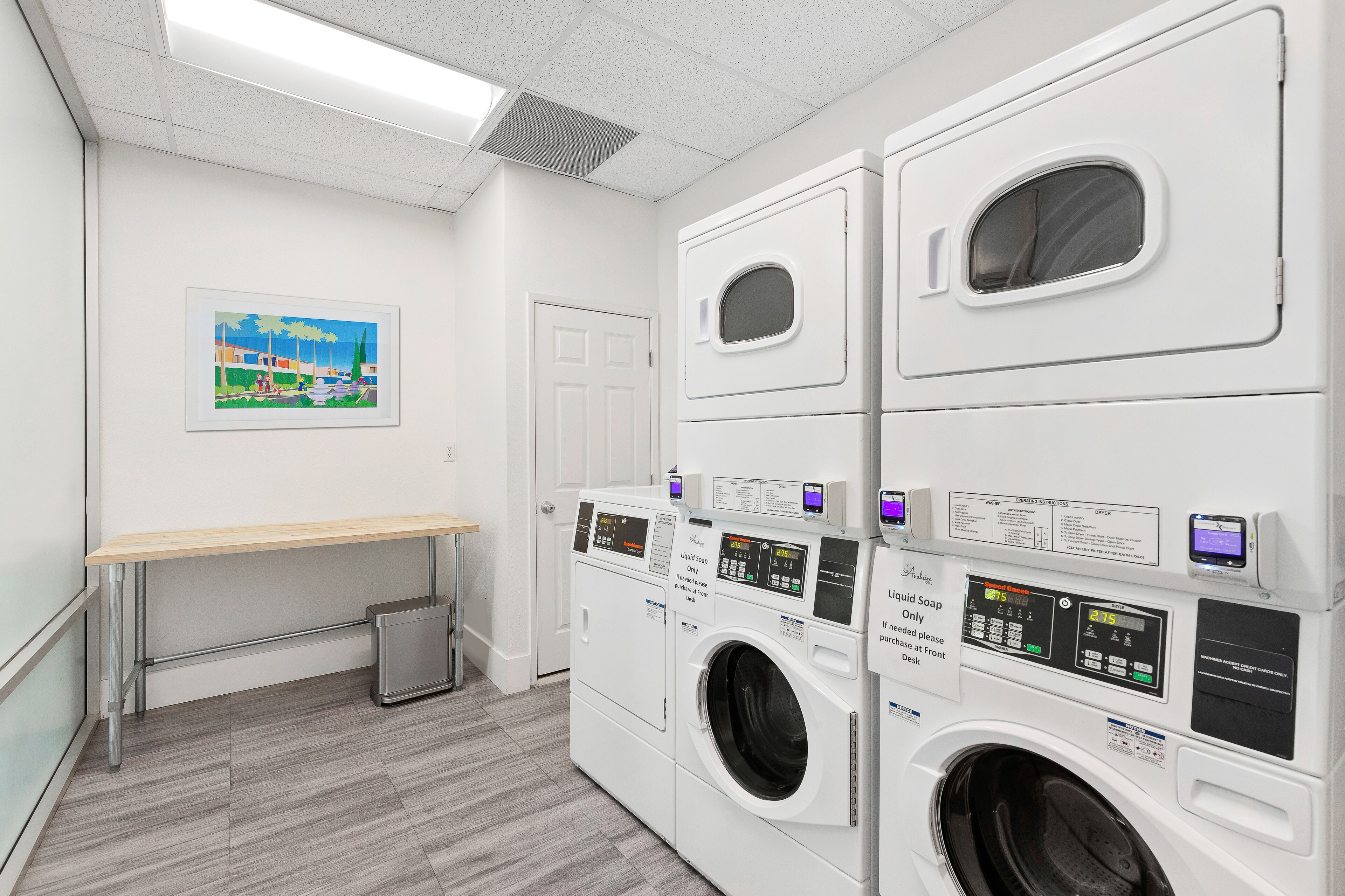 A laundry room with stacked washers and dryers, a bench, and a trash can.
