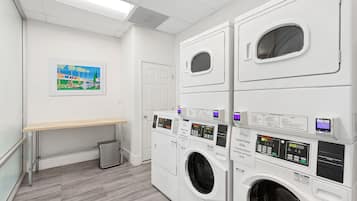A laundry room with stacked washers and dryers, a bench, and a trash can.